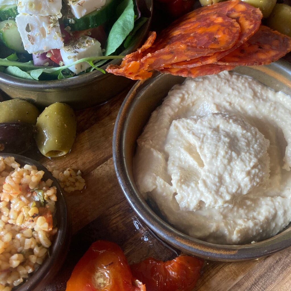 Hummus, olives, cheese and salad on a wooden board.